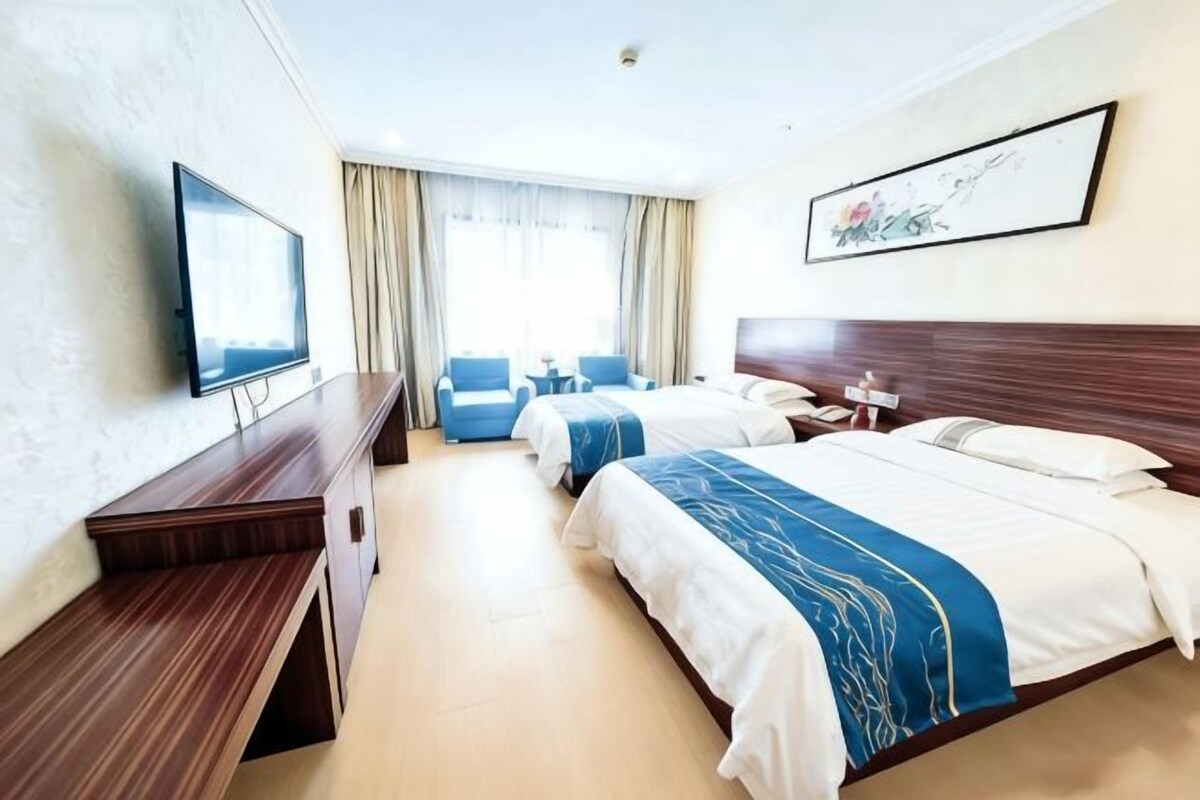 Une chambre d’hôtel avec deux lits, un bureau, une télévision et une fenêtre avec des rideaux.