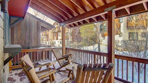 A wooden deck with rustic chairs, a lamp, and a view of buildings and trees. - 4 enSuites/2 King Beds-2 Car Garage-EZ Walk to Trails/Resort +Free Town Bus-W/D in Unit-Large Deck (Steamboat Springs)
