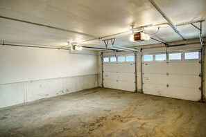 A garage with two doors, overhead lighting, and a concrete floor.