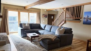 A living room with a sectional sofa, a coffee table, and a staircase with wooden railings. - 4 enSuites/2 King Beds-2 Car Garage-EZ Walk to Trails/Resort +Free Town Bus-W/D in Unit-Large Deck (Steamboat Springs)