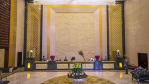 A lobby with a reception desk, a large decorative wall, and a central floral arrangement. - Taishan Bojue Hotel (Jiangmen)