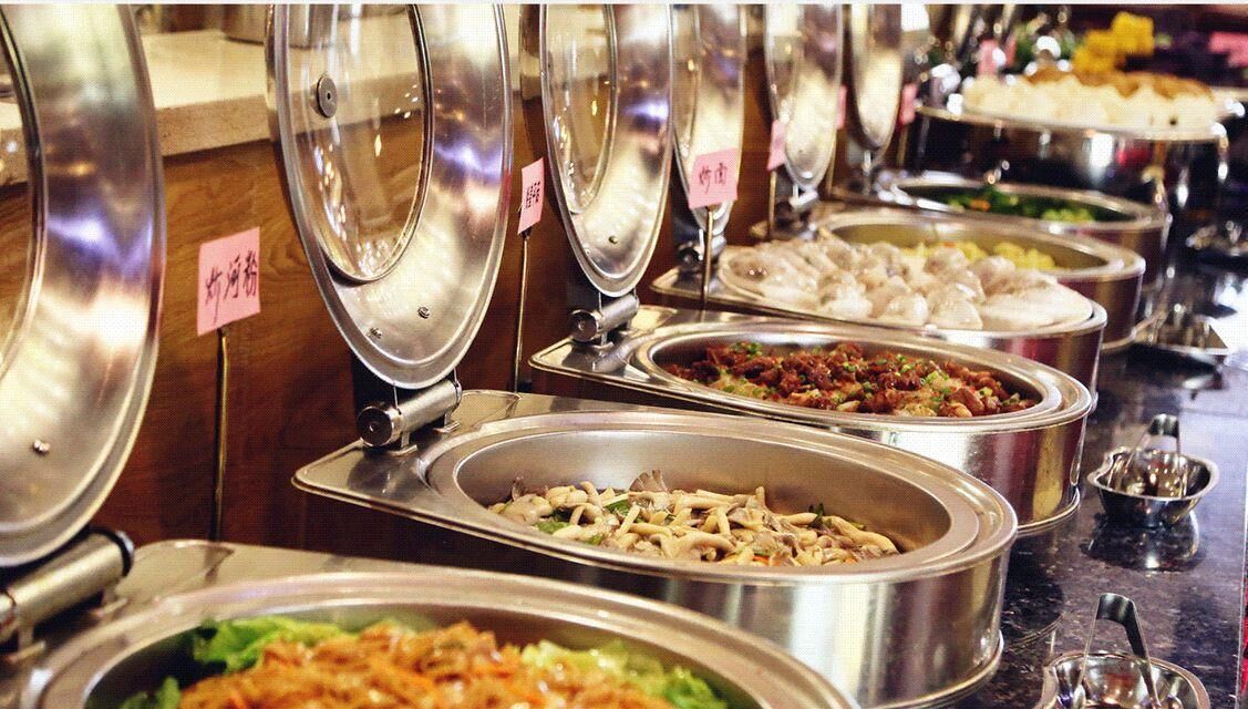 Un buffet proposant divers plats présentés dans des récipients en métal, chacun étant muni d’une étiquette.