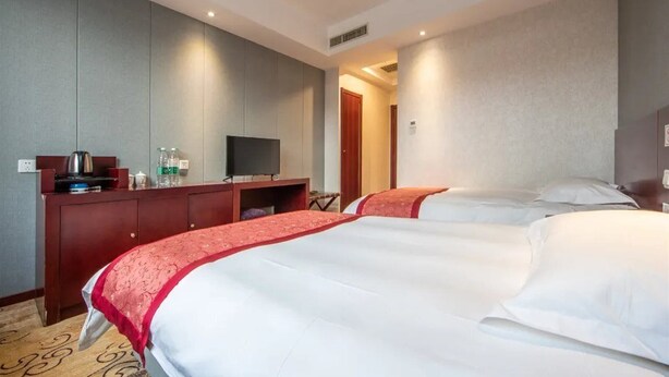 Ein Hotelzimmer mit zwei Betten, einem Fernseher, einem Schreibtisch mit Computer und einer Minibar.