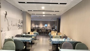 Un comedor con mesas y sillas, una cocina al fondo, y una pared decorada con obras de arte.