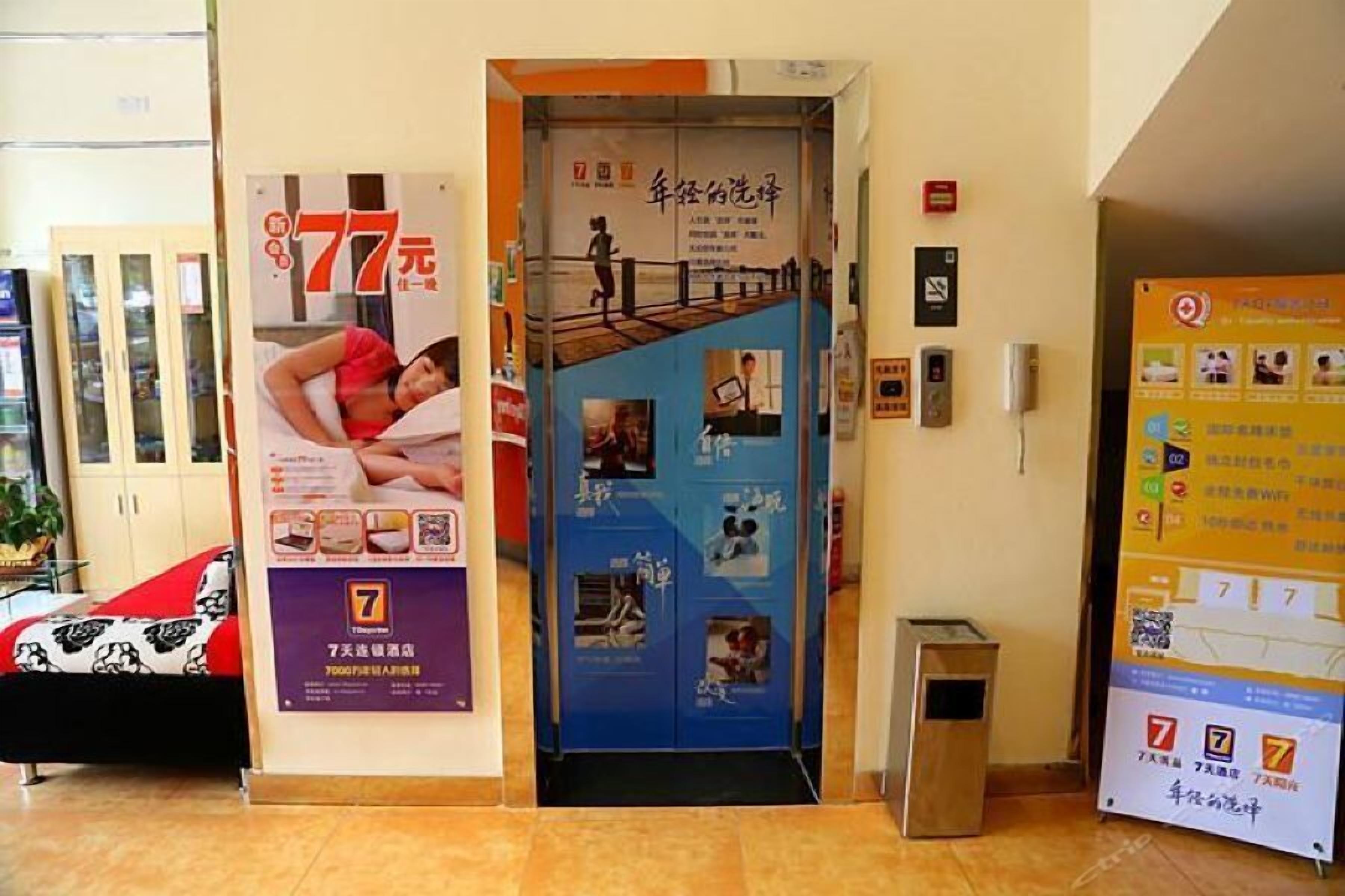 Un hall d’hôtel avec une porte d’entrée bleue, une affiche faisant la promotion d’une offre à 77 yuans, et une petite poubelle placée à droite.