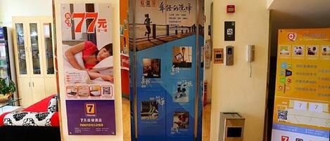 Un hall d’hôtel avec une porte d’entrée bleue, une affiche faisant la promotion d’une offre à 77 yuans, et une petite poubelle placée à droite.