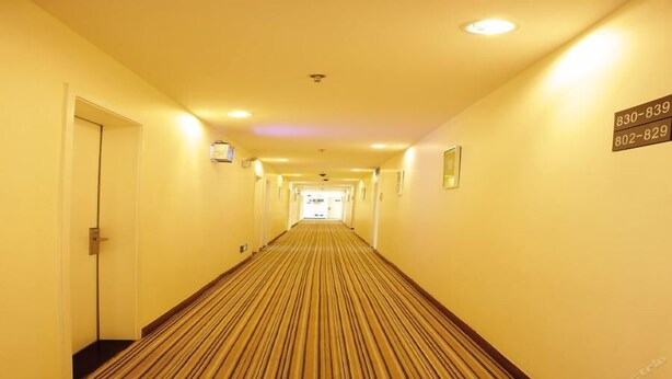 Un pasillo de hotel con alfombra a rayas, puertas a ambos lados y un letrero con números de teléfono.