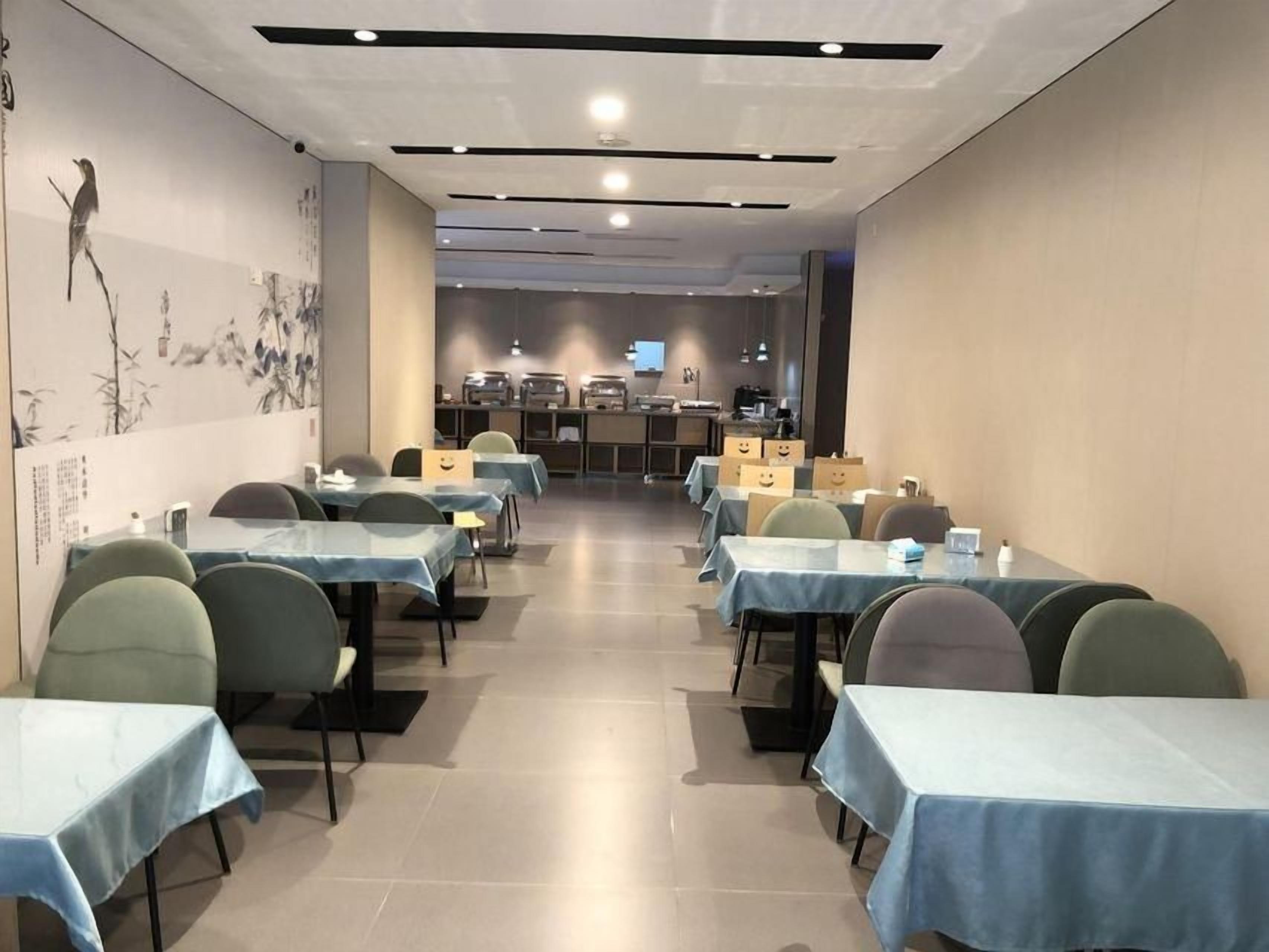 A dining area with tables and chairs, a kitchen in the background, and a wall with artwork.