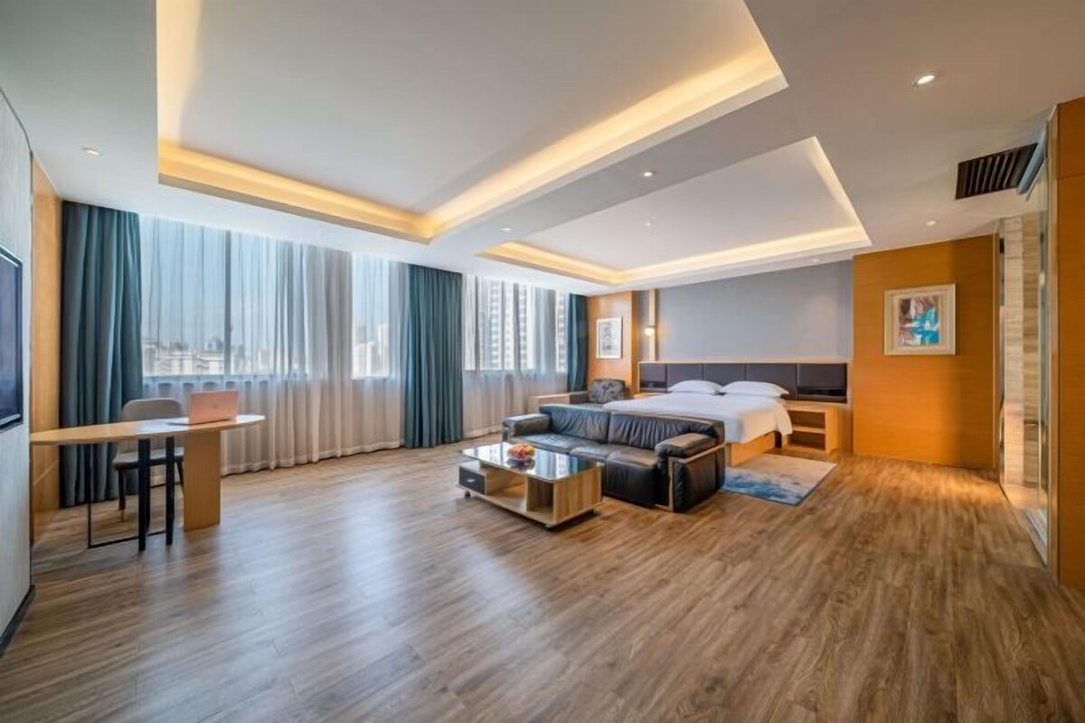 A modern hotel room with a bed, a sofa, a coffee table, and a desk.