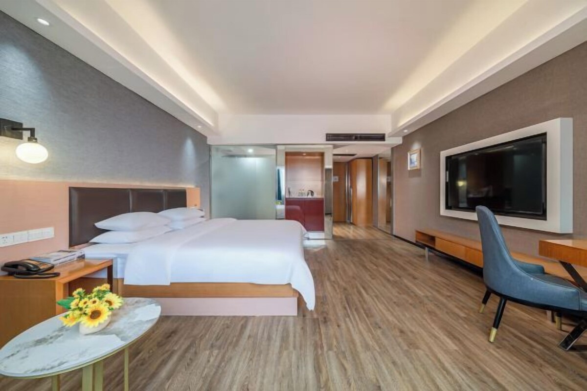 Una habitación de hotel moderna con una cama grande, un escritorio con teléfono, un televisor montado en la pared y una zona de estar con una silla.