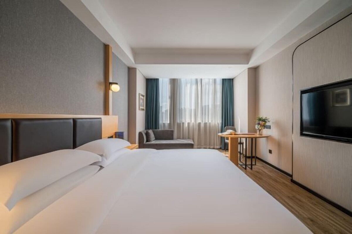 Habitación de hotel con una cama grande, un escritorio, una silla, un televisor y una ventana con cortinas.