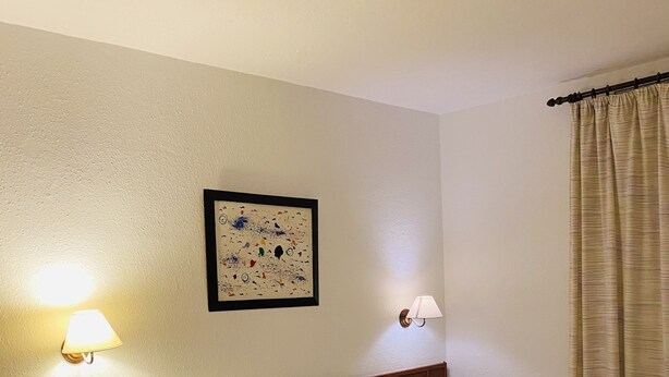 Une chambre d’hôtel avec un lit soigneusement fait, deux tables de chevet, un tableau accroché au mur et deux appliques murales.