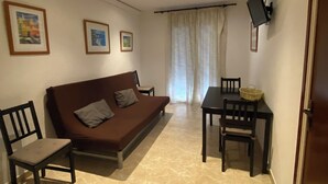 Un salon avec un canapé marron, une table à manger avec des chaises, un téléviseur fixé au mur et des tableaux encadrés accrochés au mur.