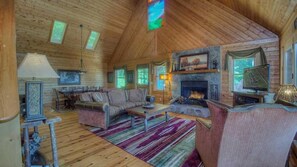 A cozy log cabin interior with a fireplace, a dining area, and a comfortable seating arrangement. - Grand View - Mountain View | Hot tub | Shuffleboard | Air Hockey | Screened in porch (Blue Ridge)