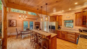 A spacious kitchen with wooden cabinets, a large island with bar stools, and a dining area with a bench. - Heaven on the Lake - Lakefront | Hot Tub | Fire Pit | Game Room (Blue Ridge)