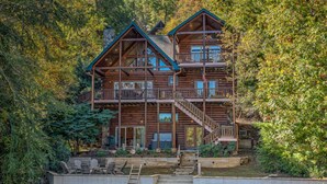 A multi-story log cabin with a balcony, surrounded by dense forest. - Heaven on the Lake - Lakefront | Hot Tub | Fire Pit | Game Room (Blue Ridge)