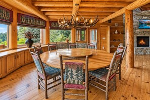 Uma sala de jantar de madeira com uma mesa redonda e cadeiras, lareira e vista para o exterior.