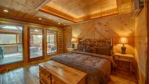 A log cabin bedroom with a large bed, wooden floors, and a balcony with sliding glass doors. - Lonesome Dove - Custom Western Style Log Lodge | Screened in outdoor living (Blue Ridge)