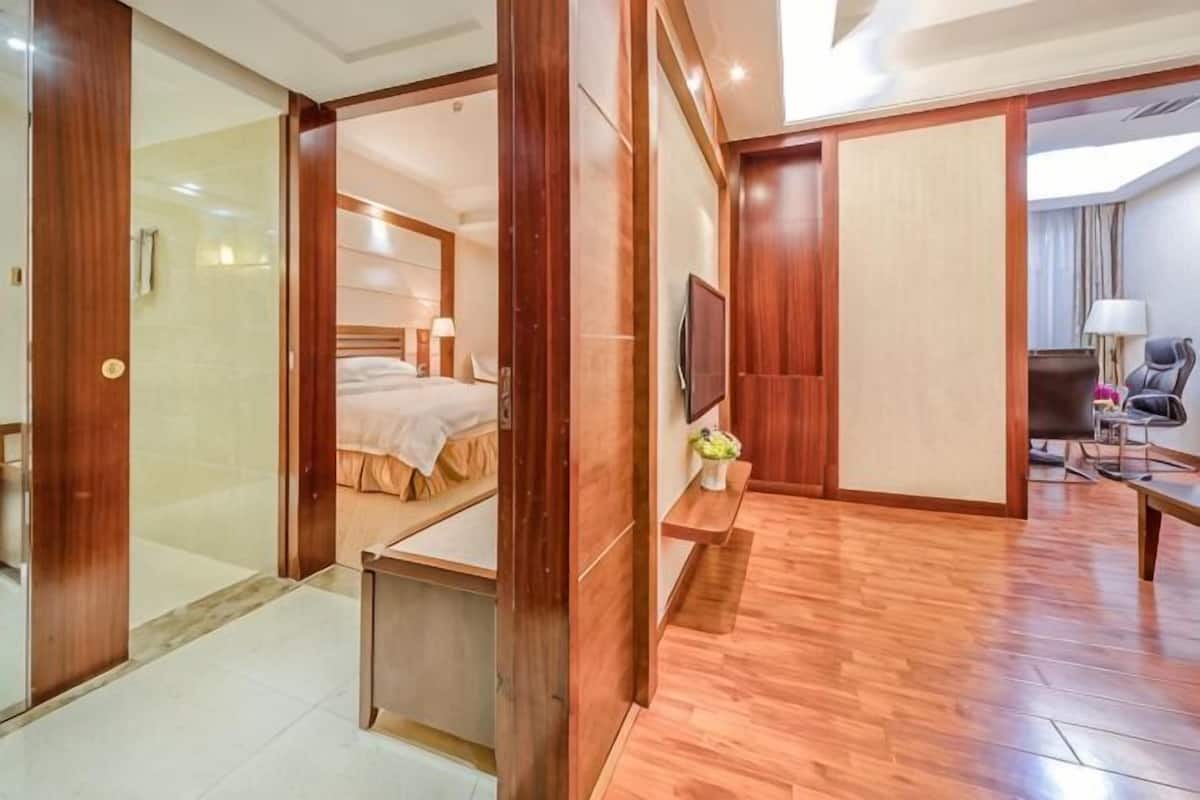 Ein Hotelzimmer mit Holzboden, einem Bett, einem Fernseher, einem Schreibtisch und einem Sessel.