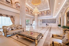 A luxurious lobby with ornate furniture, a grand chandelier, and classical artwork.