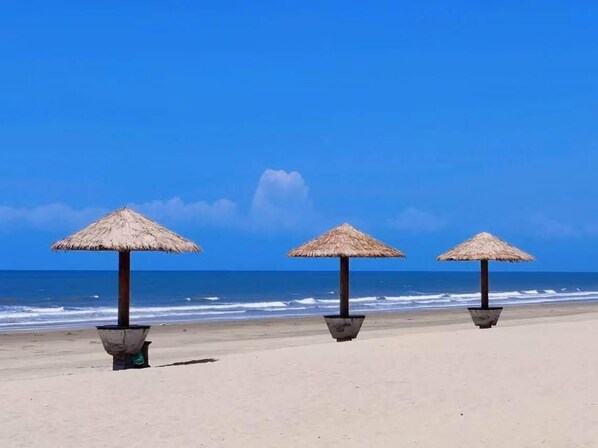 A beach with three thatched umbrellas and a clear blue sky.