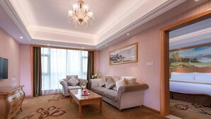 A hotel room with a large bed, a sofa, a coffee table, a TV, and a painting on the wall. - Vienna International Hotel (Maoming)
