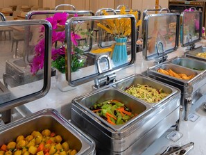 A buffet setup with various food items in metal containers, including salads, vegetables, and possibly some fried items.
