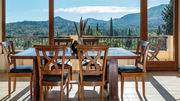 Uma sala de jantar com mesa e cadeiras de madeira, grandes janelas e vista para as montanhas.
