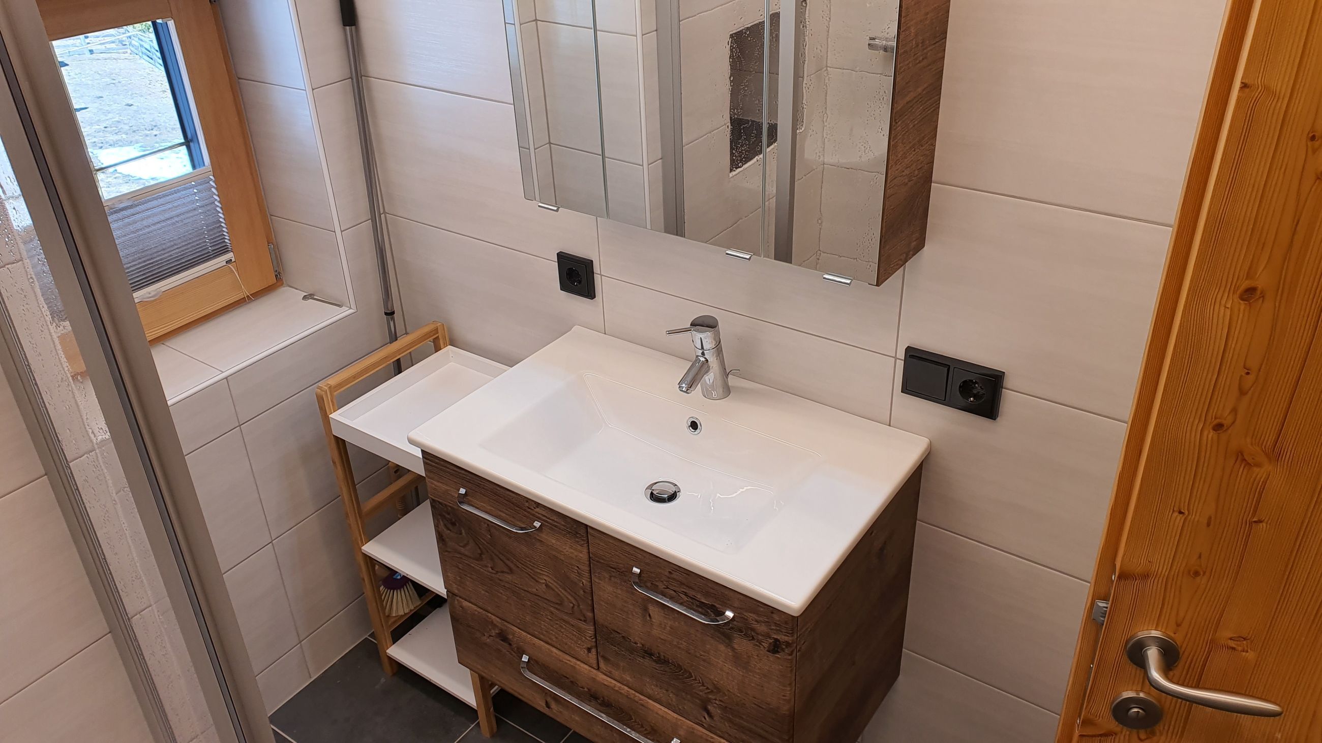 A bathroom with a white sink, wooden vanity, a mirror, and a window.