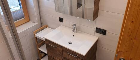 A bathroom with a white sink, wooden vanity, a mirror, and a window.