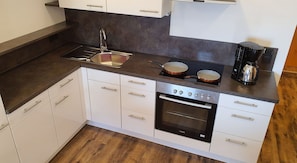 A modern kitchen with white cabinets, a stainless steel sink, a stove, and a coffee maker.