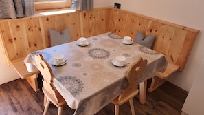 A wooden dining table with a patterned tablecloth, surrounded by wooden chairs and benches.