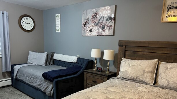 A bedroom with two beds, a clock, a motivational quote, and a floral painting. - Just Like Being At Home- Newly Renovated Unit (North Troy)