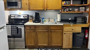 A kitchen with wooden cabinets, a microwave, a stove, a coffee maker, a toaster, and a sink. - Just Like Being At Home- Newly Renovated Unit (North Troy)