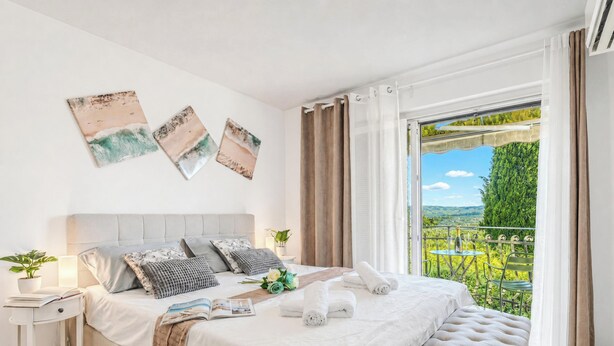 A bedroom with a bed, pillows, a bedside table with a lamp, a window with curtains, and a view of greenery outside. - House In The Vineyards Ankaran (Ankaran)