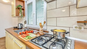 A kitchen with a gas stove, a cutting board with vegetables, a kettle, and a window with blinds. - House In The Vineyards Ankaran (Ankaran)