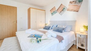 A bedroom with a bed, pillows, a bedside table, a nightstand, and wall art. - House In The Vineyards Ankaran (Ankaran)