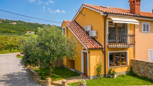 A yellow house with a tiled roof, a balcony, and a stone wall. - House In The Vineyards Ankaran (Ankaran)