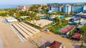 Vista aèria d'una estació turística a la costa, amb una platja, diversos edificis d'hotel i una pista de tennis.