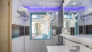 Une salle de bain moderne avec un grand miroir, une baignoire et une fenêtre donnant sur une chambre.