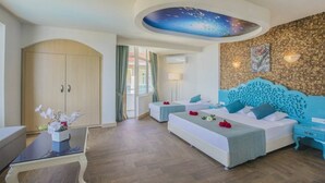 Une chambre d’hôtel avec un grand lit, un lit plus petit, une armoire, une table en verre avec un vase et un plafond décoratif.