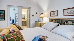 A hotel room with a bed, pillows, a nightstand with a lamp, framed pictures on the wall, and a view of the hallway. - Country Lemonvilla (Massa Lubrense)