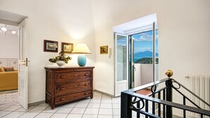 A room with a wooden dresser, a lamp, framed pictures, and a view through a glass door to the outside. - Country Lemonvilla (Massa Lubrense)