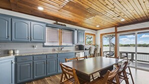 Cocina moderna con armarios azules, una mesa de comedor de madera y vistas a un lago a través de amplios ventanales.