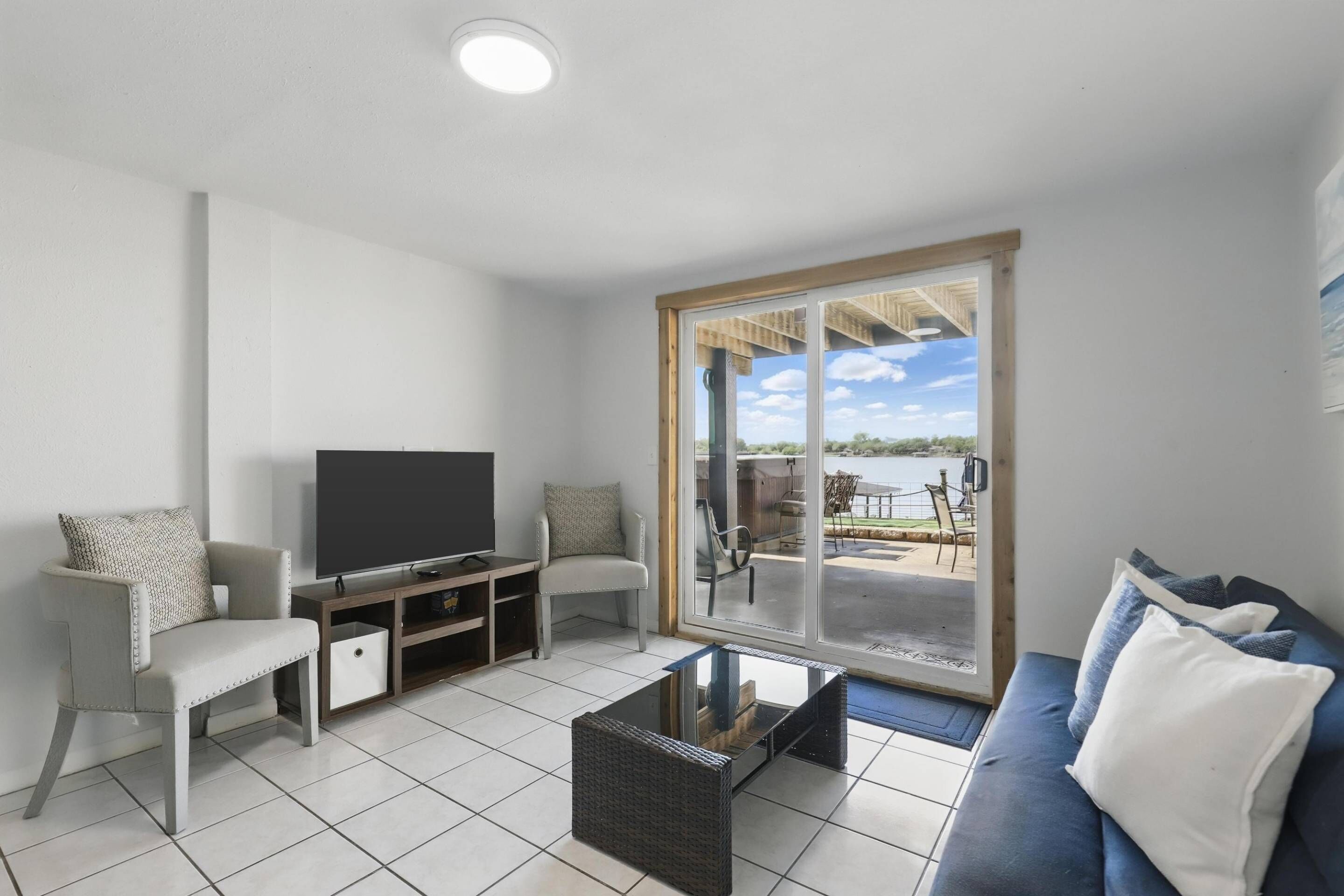 Ein modernes Wohnzimmer mit Flachbildfernseher, einer Couch, einem Couchtisch und einer Glasschiebetür, die auf eine Terrasse im Freien führt.
