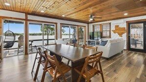 Una habitación amplia con techo de madera, ventanas grandes, una mesa de comedor con sillas, un sofá y un sillón colgante.