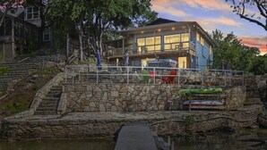 Una propiedad frente al agua con una escalera de piedra que conduce a una terraza, un muelle y un edificio con amplios ventanales.