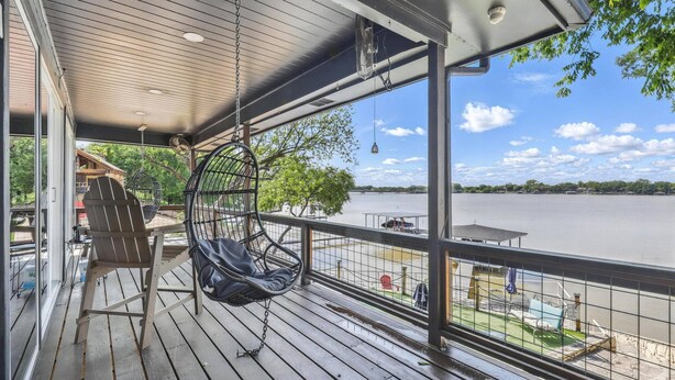 Una terraza de madera con una hamaca colgante, una mesa y vistas a un lago.