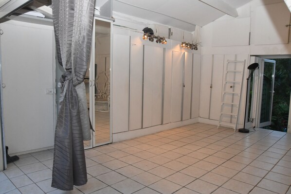 A room with a tiled floor, a white wardrobe, a ladder, and a door leading outside.