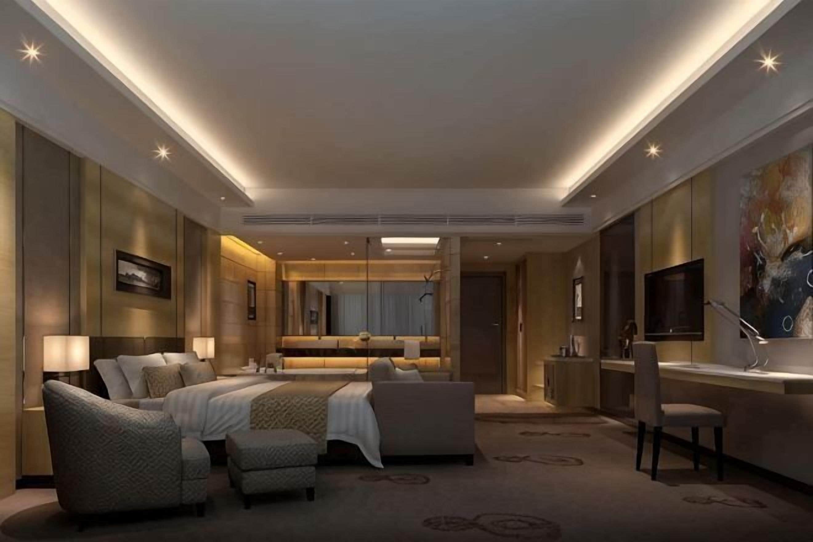 Una habitación de hotel moderna con una cama grande, una zona de estar, televisión y un baño con espejo y lavabo.